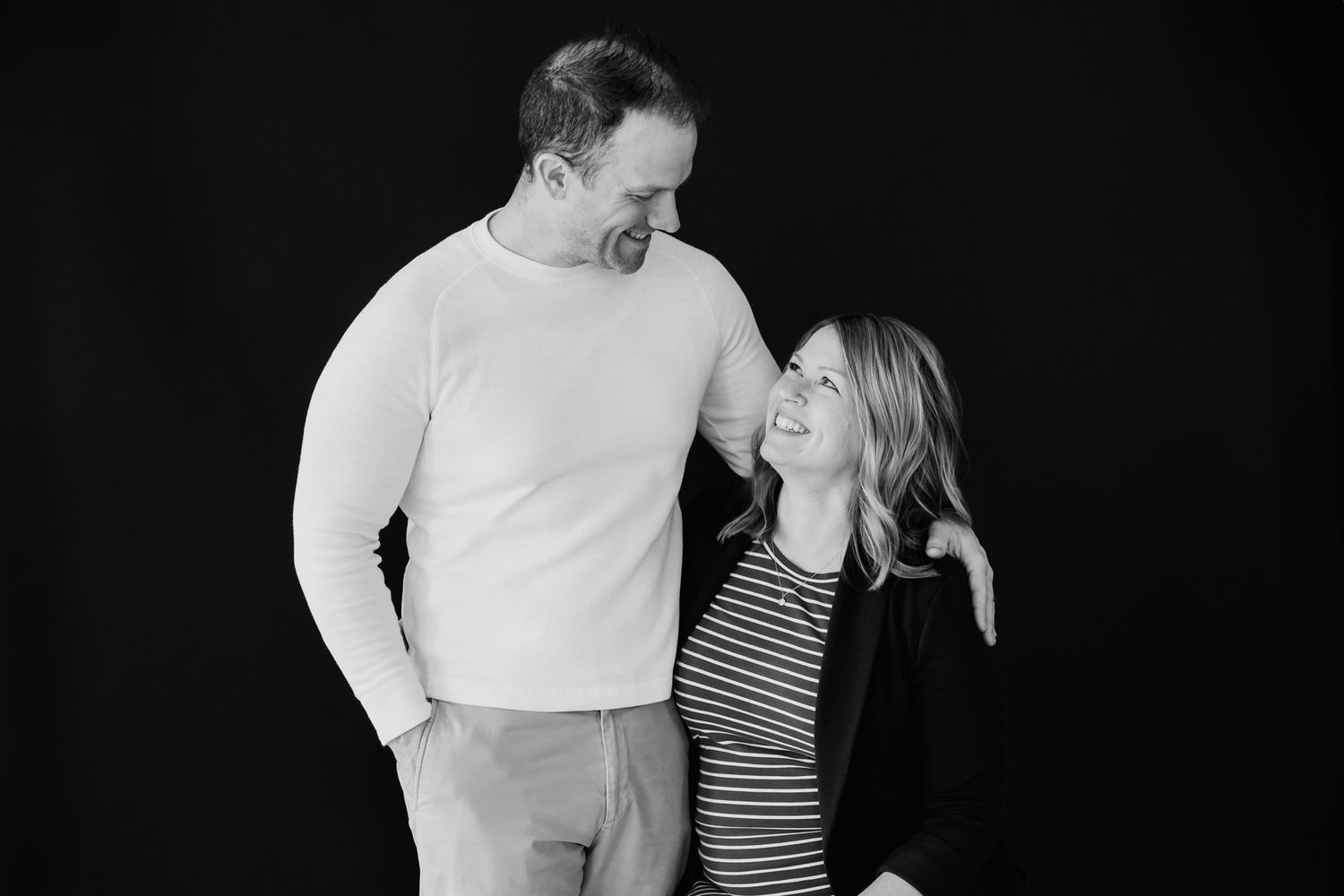 Black and white photo of a couple smiling at each other during a maternity portrait session.