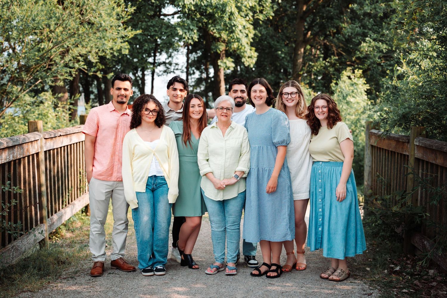 Smiling multigenerational family posing together on a wooden bridge with green trees in background.