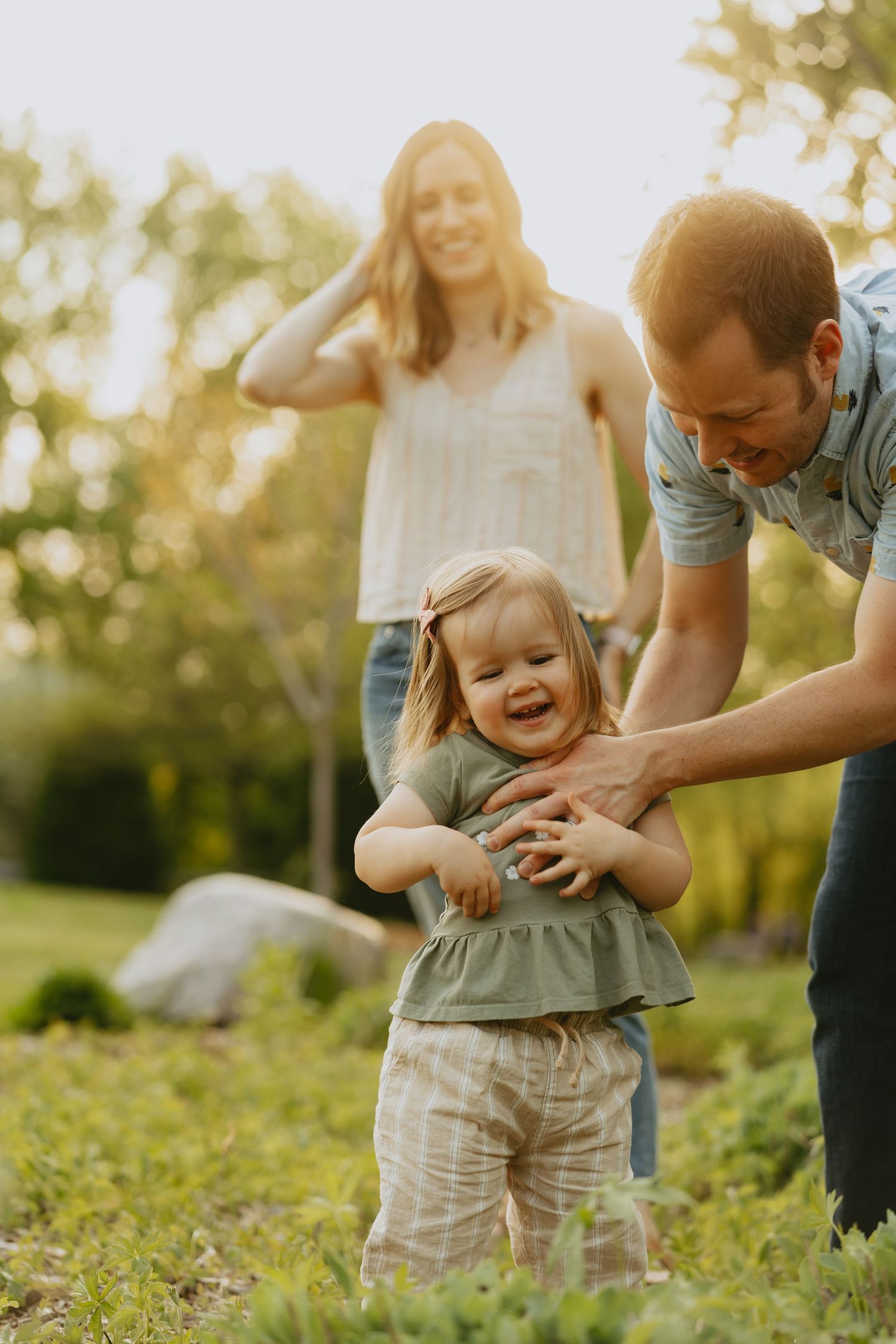 Dad tickling daughter, mom standing behind them