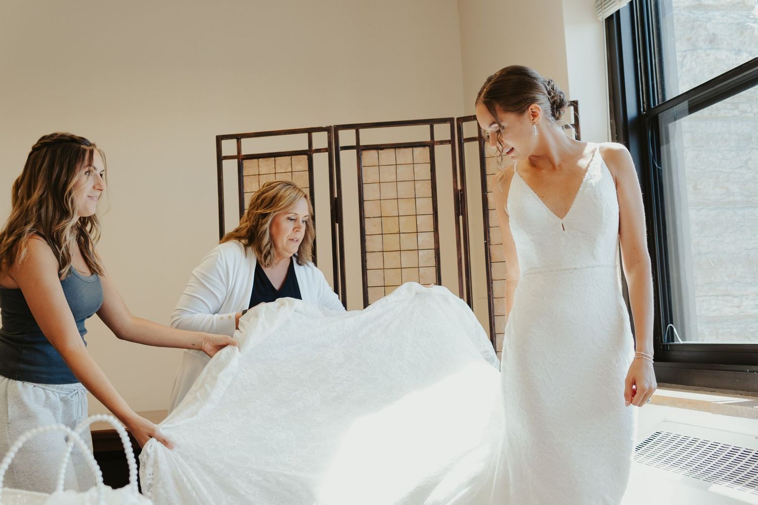 Bride's mother and sister help adjust her dress.