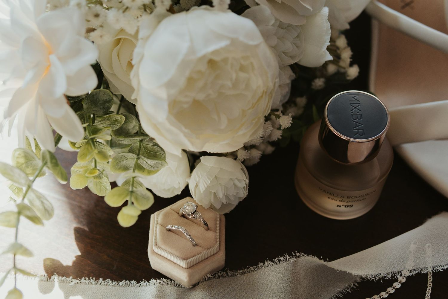 Flat lay image of rings, perfume, and flowers.