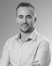 Professional headshot of a young smiling businessman with arms crossed in a black and white portrait photo.