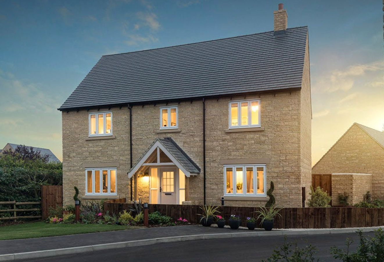 A charming two-story stone cottage-style new build home with warm interior lighting at dusk, featuring a slate roof.