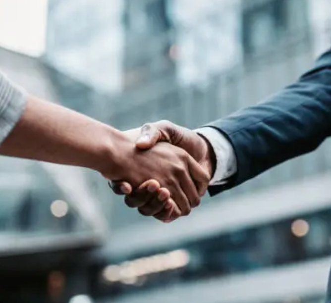 Two professionals shaking hands outdoors with a modern glass building in the background, symbolizing a business agreement.