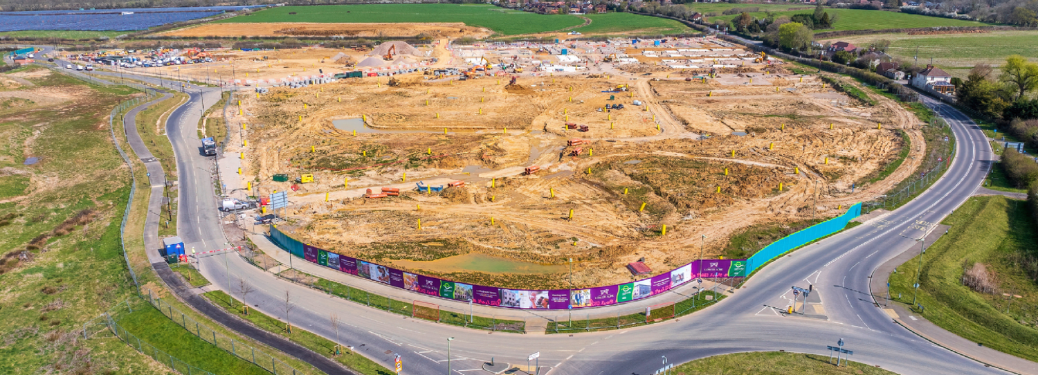 Aerial panoramic view of a large construction site with colorful hoardings near a coastal road in Ireland.