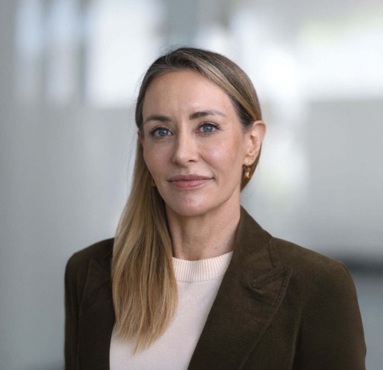 Professional woman with long blonde hair wearing a dark blazer and white top poses for a corporate headshot.