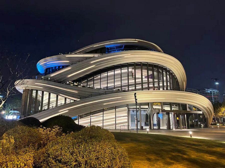 Futuristic spiral building with curved silver facades illuminated at night, showcasing modern architectural design.