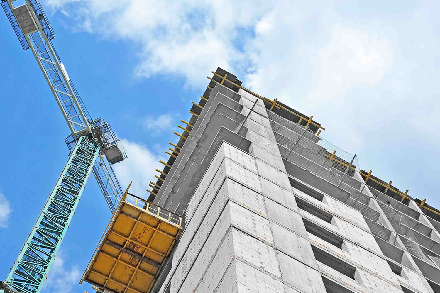 High-rise concrete building under construction with tower crane against blue sky.