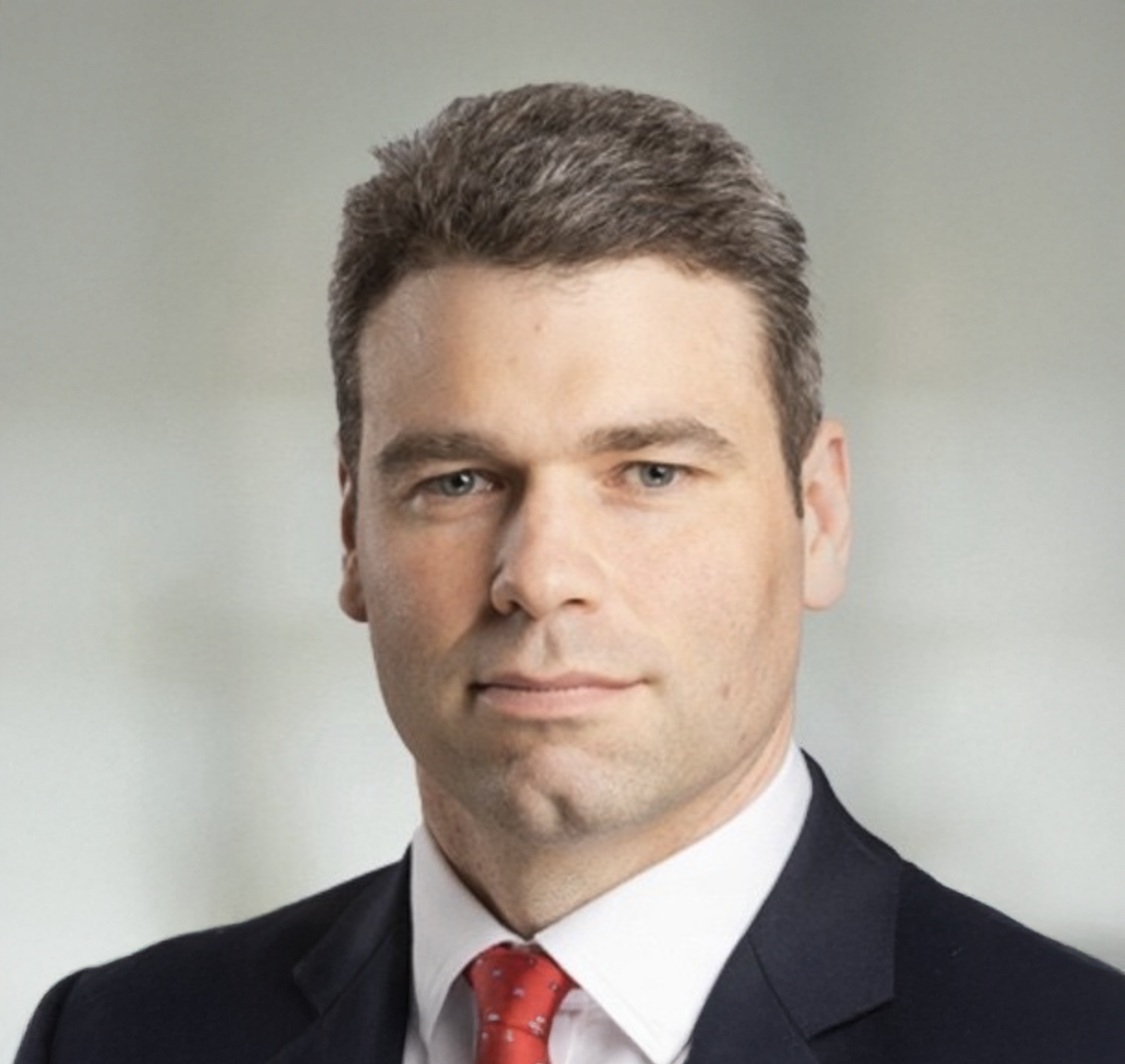 Professional businessman in dark suit and red tie poses for formal corporate headshot portrait photo.