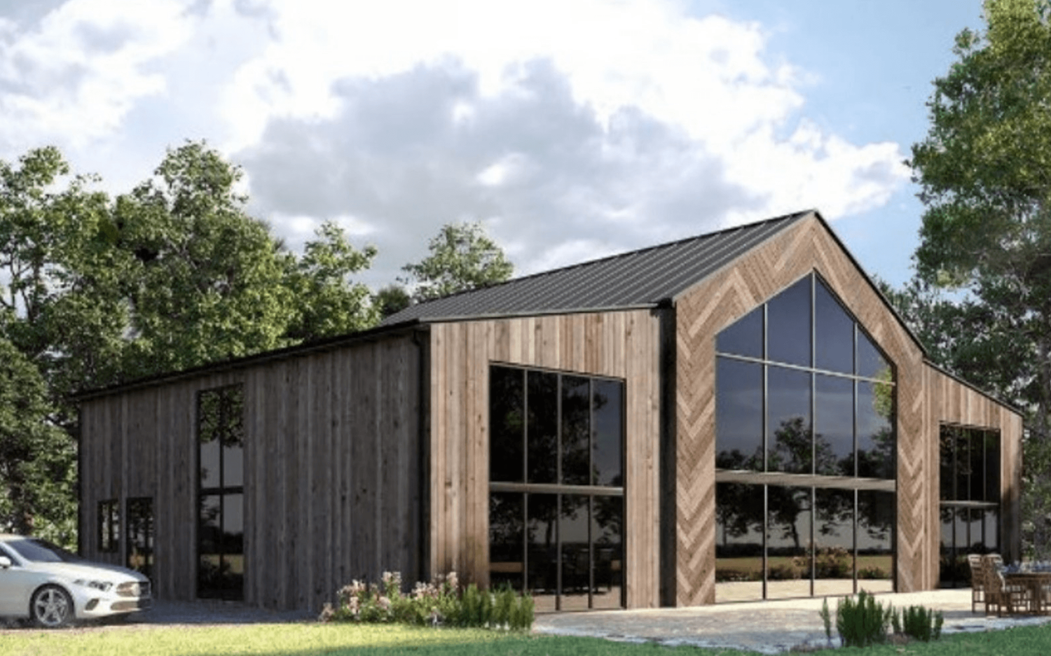 Modern barn-style building with wood cladding, black metal roof, and large glass facade surrounded by trees.