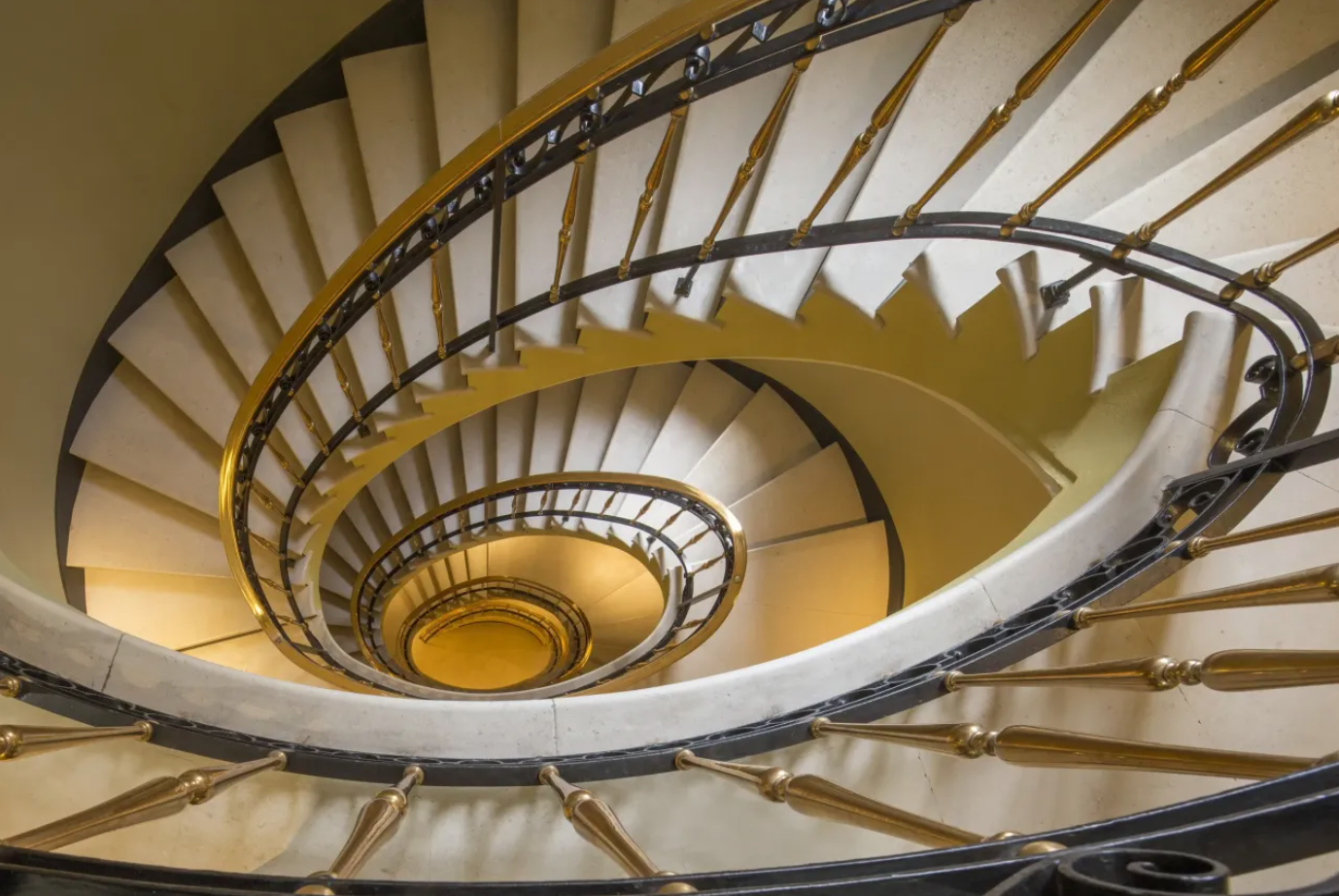 Stunning aerial view of an elegant spiral staircase with golden steps and ornate iron railings in a classic building.