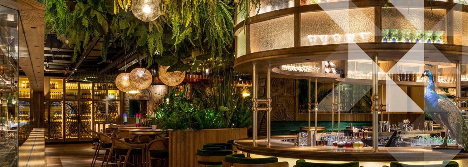 Elegant restaurant interior with lush greenery, warm pendant lights, wooden accents, and a decorative peacock display.