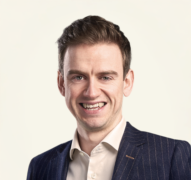 Young professional man in navy pinstripe blazer smiling confidently against light background.