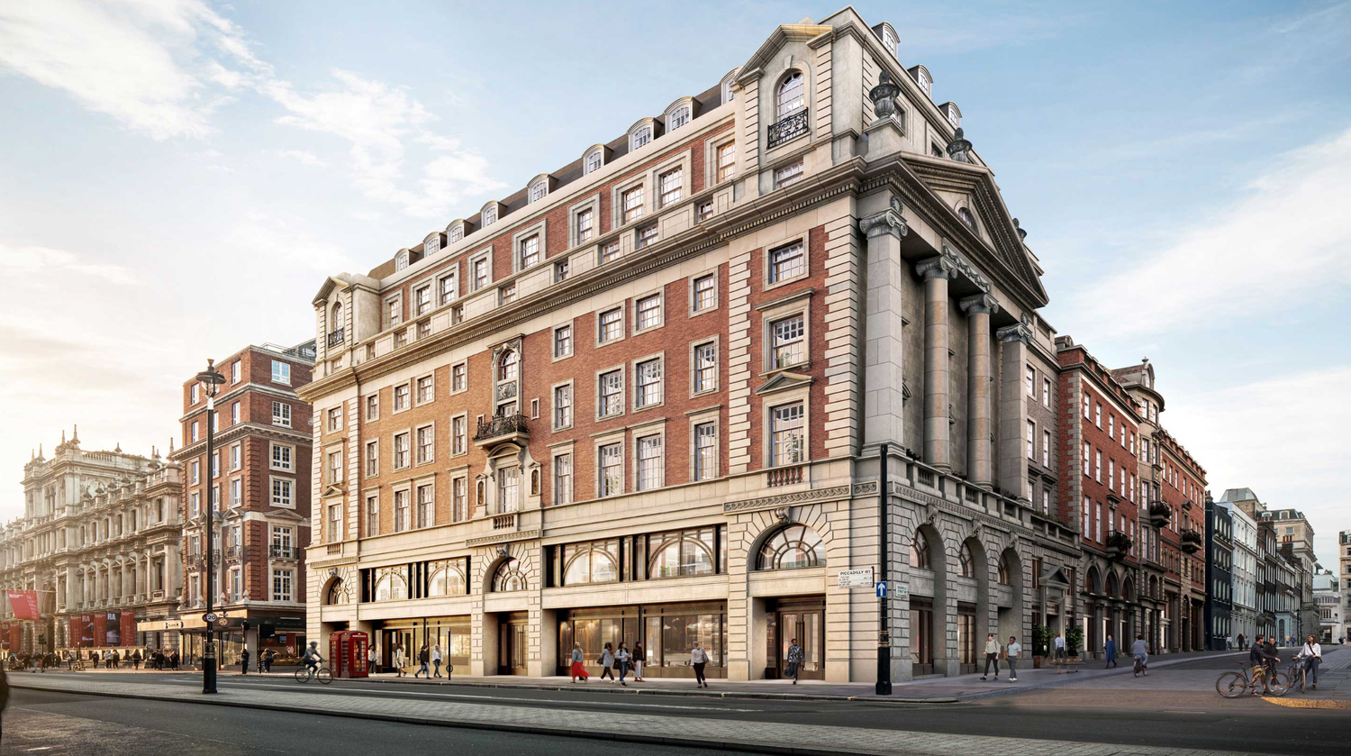 Grand historic red brick building on a London street corner with classical architectural details and ground-floor retail spaces.