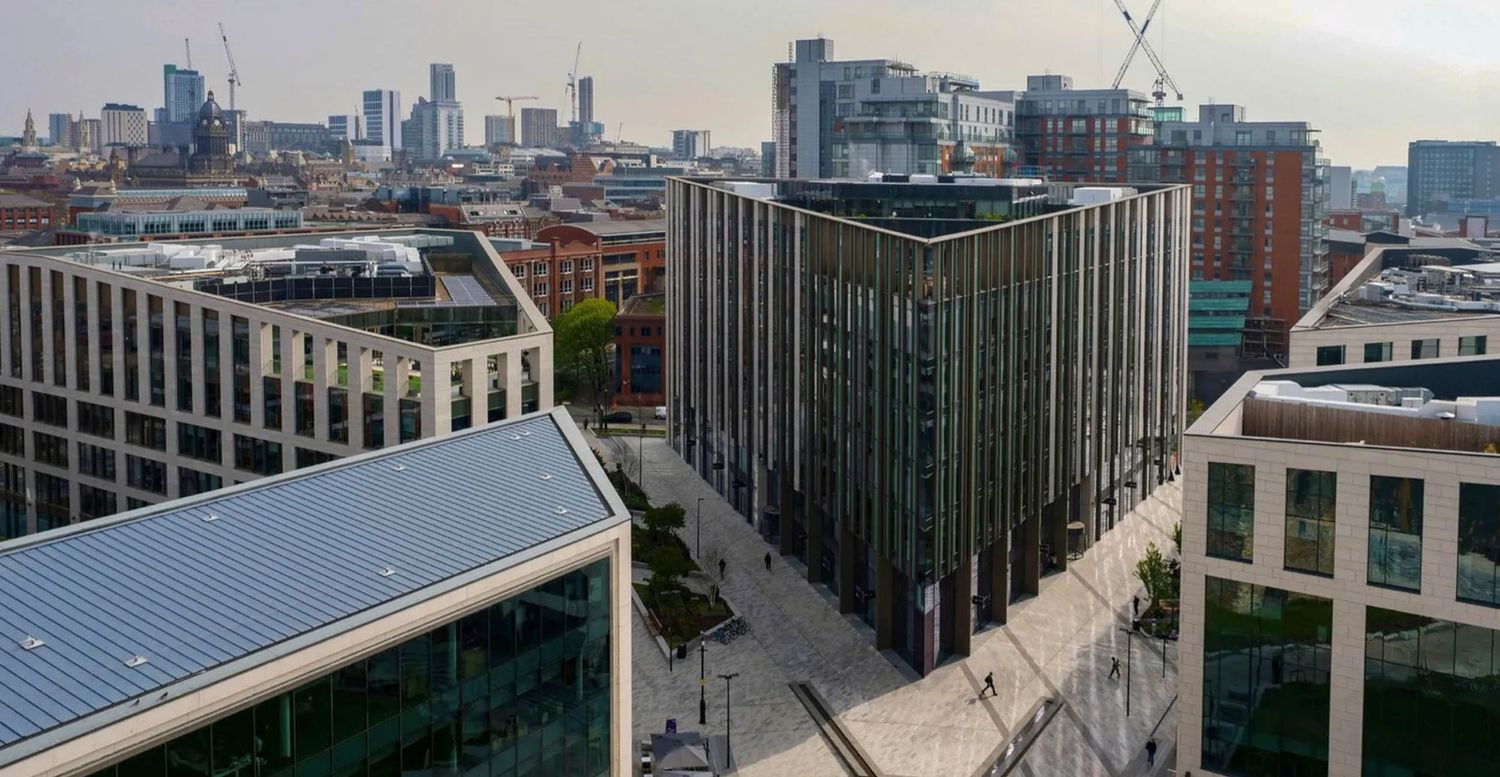 Aerial view of modern glass office buildings in an urban city center with skyline and construction cranes in background.