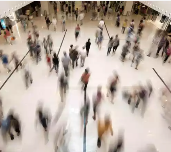 Aerial view of a busy shopping mall atrium with blurred crowds of people walking on a white floor.