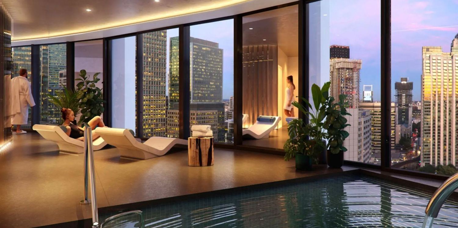 Luxury rooftop indoor pool with city skyline views at dusk, featuring lounge chairs and lush greenery.