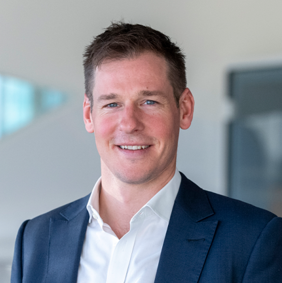Professional businessman in navy blazer smiling confidently in modern office setting, corporate headshot photo.