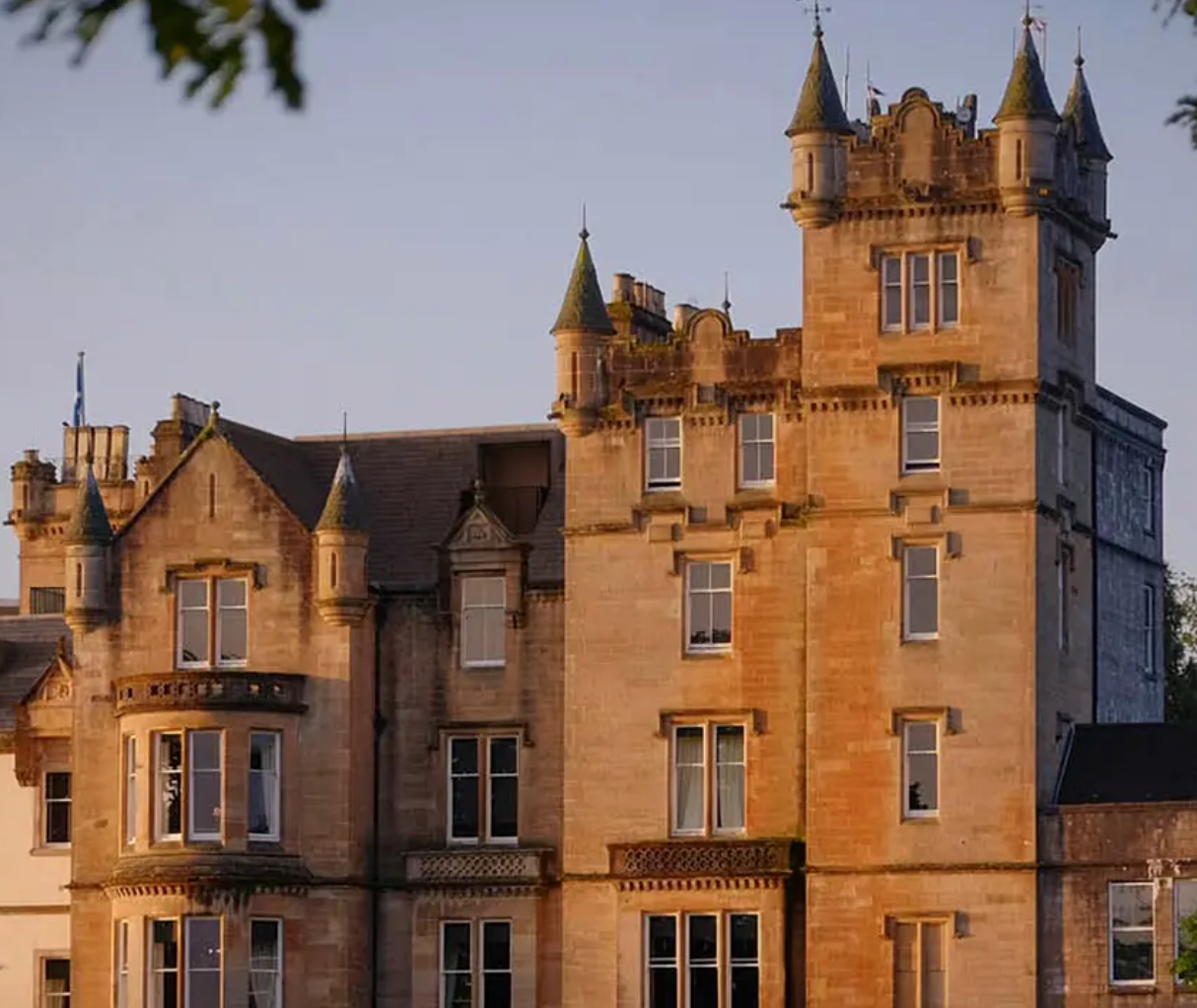 Historic Scottish castle hotel with ornate stone towers and warm golden facade glowing in evening light.