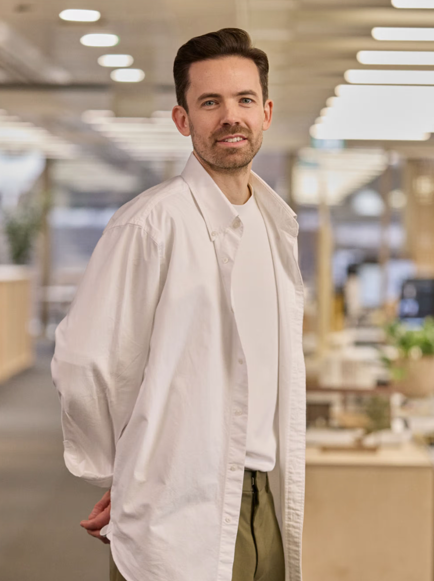 Man in white chef coat smiling, standing in modern restaurant interior.