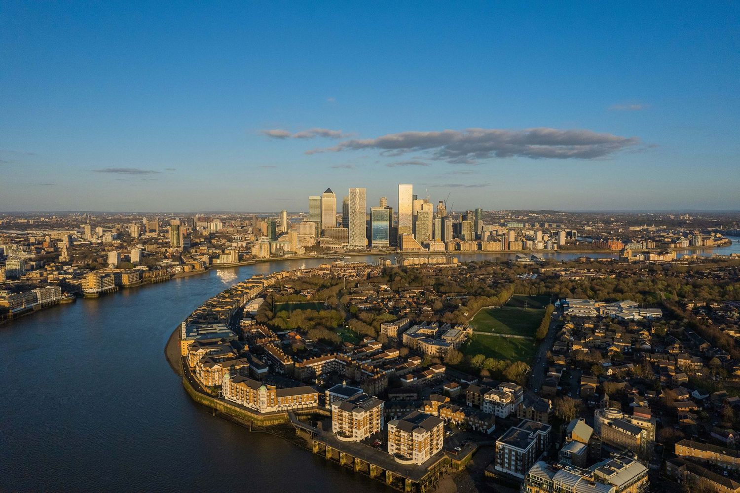 Aerial view of London's Canary Wharf skyline along the River Thames at golden hour.