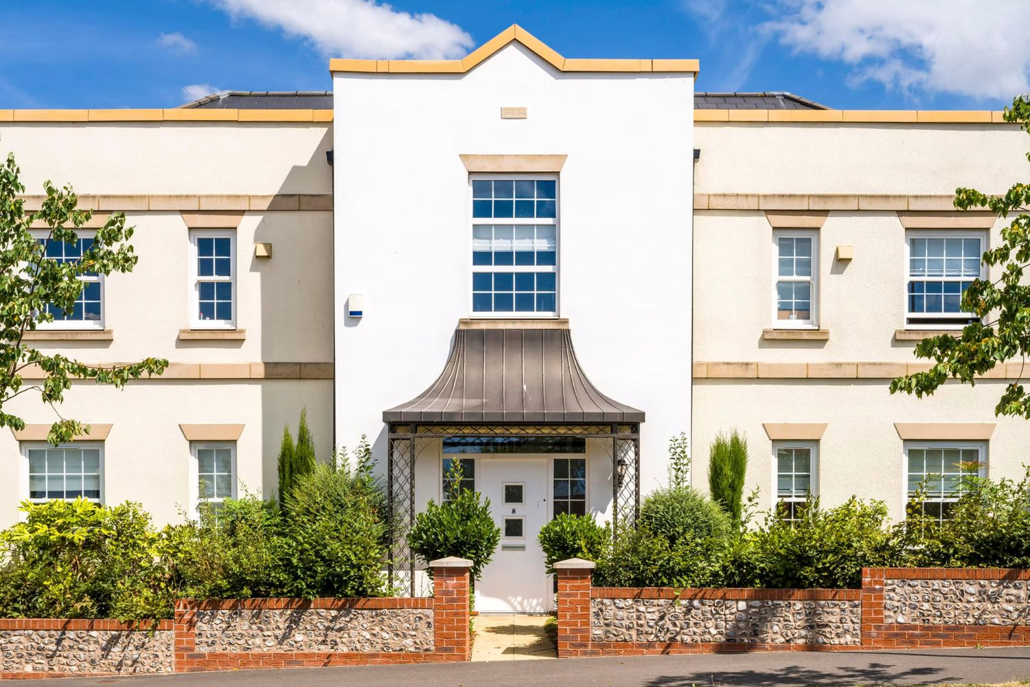 White Georgian-style townhouse with elegant portico entrance, manicured hedges, and symmetrical sash windows under a blue sky.