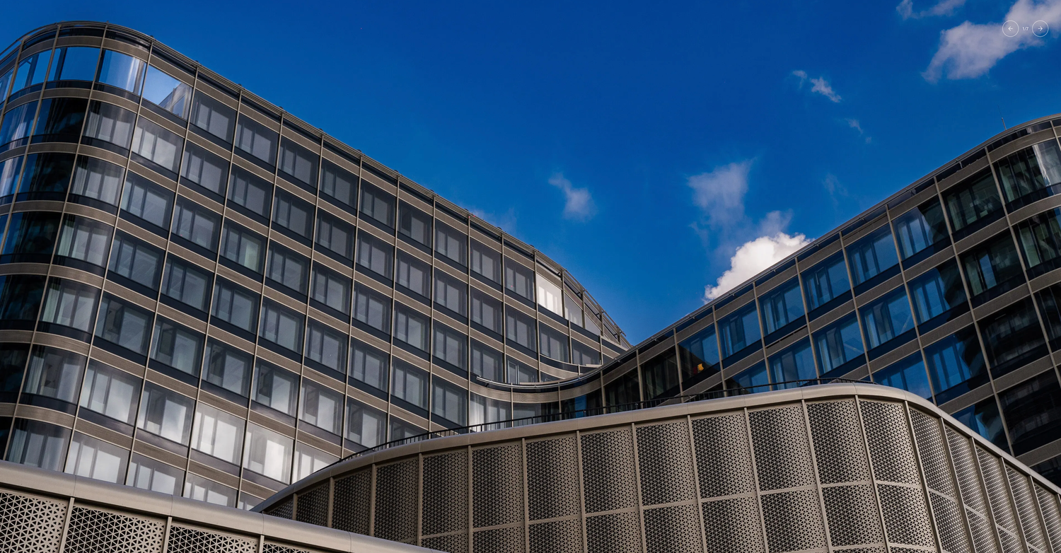 Modern curved glass office building facade against blue sky with white clouds in urban architecture.