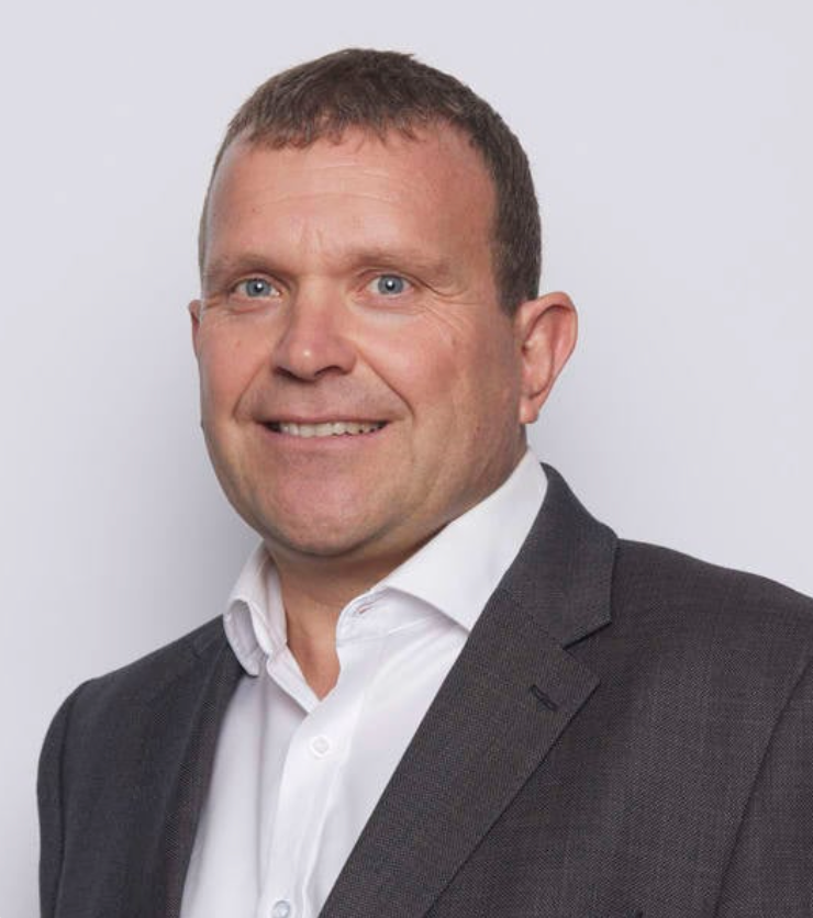Professional headshot of a smiling middle-aged businessman in a gray suit and white shirt against a light background.