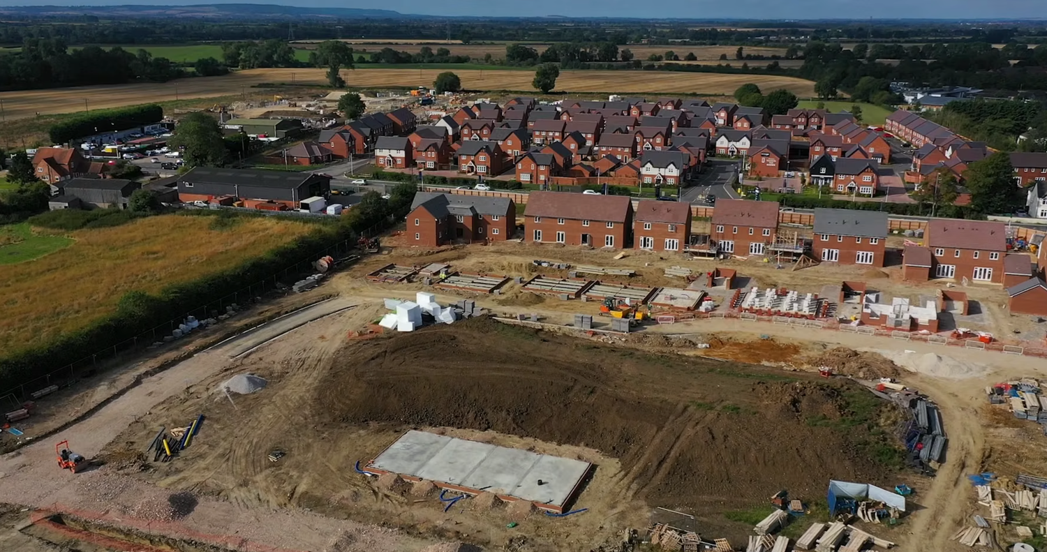 Aerial view of a UK residential housing development under construction with completed brick homes and active building site.