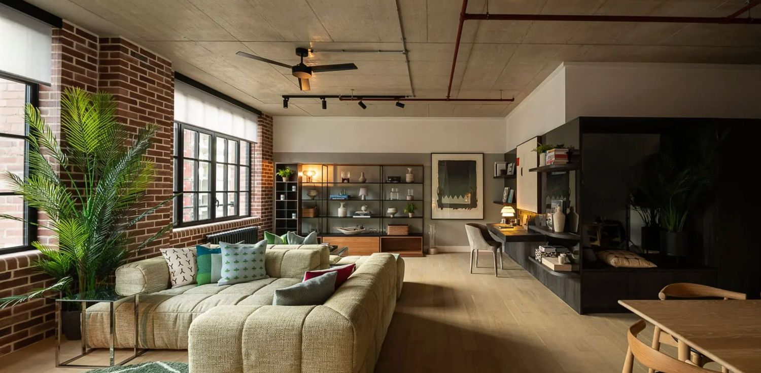 Industrial loft living room with exposed brick walls, green sectional sofa, indoor plants, and modern track lighting.