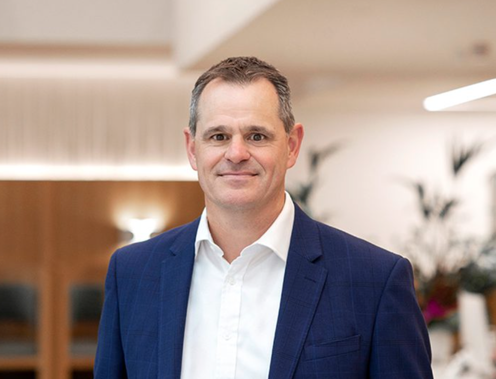 Professional businessman in blue blazer smiling confidently in a modern office environment.