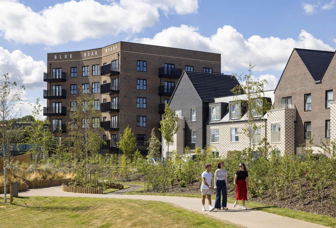 Modern residential apartment complex with landscaped gardens and a family walking along a pathway on a sunny day.