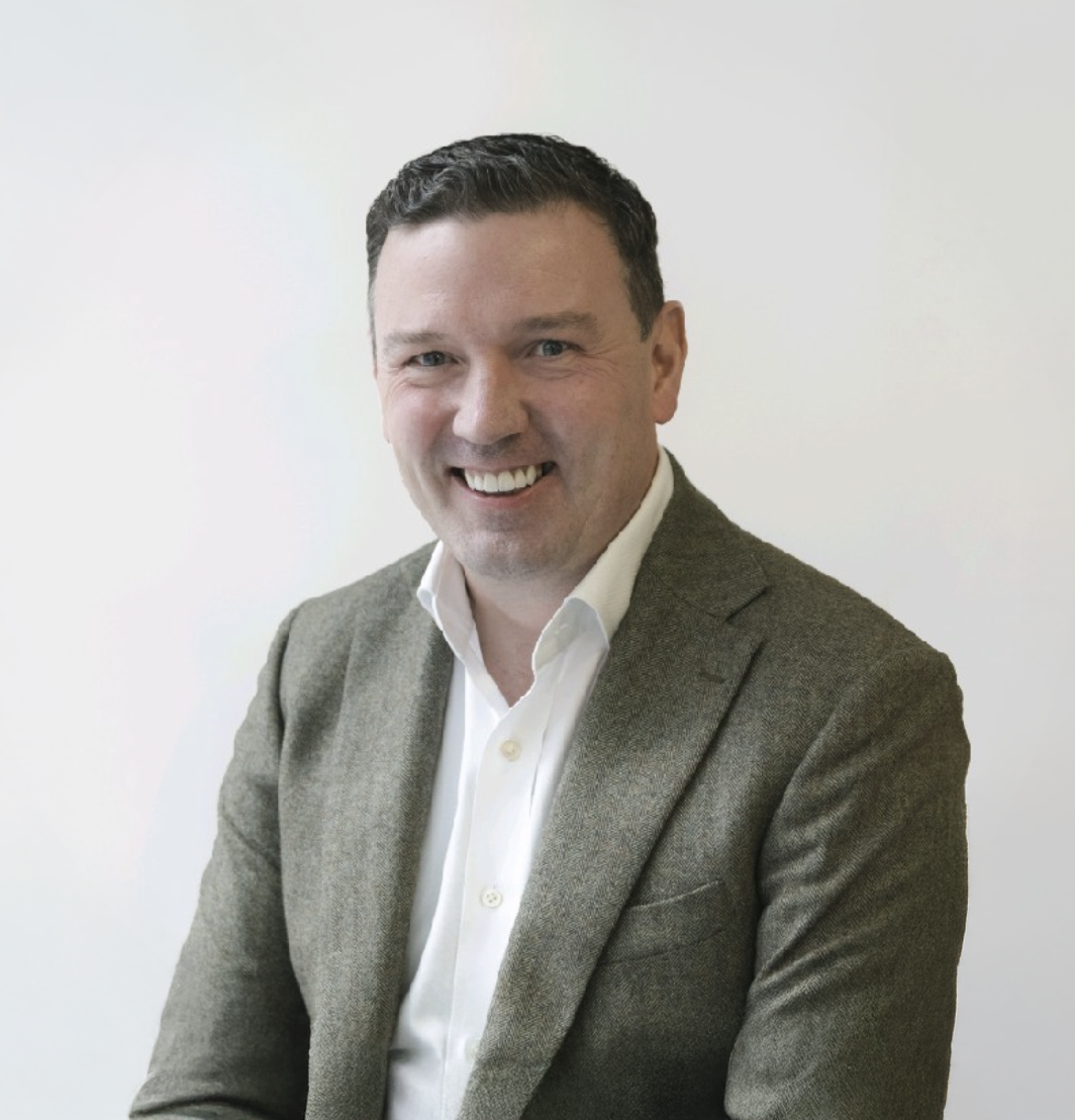 Smiling businessman in a gray blazer and white shirt poses confidently against a light background.