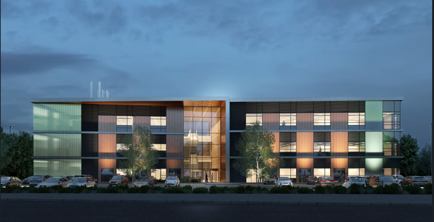 Modern three-story commercial office building exterior illuminated at dusk with colorful facade panels and landscaping.