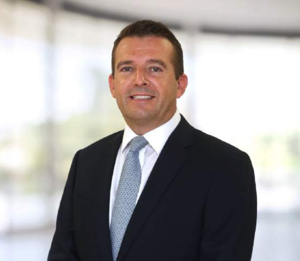 Professional businessman in dark suit and tie smiling confidently in a modern office setting.