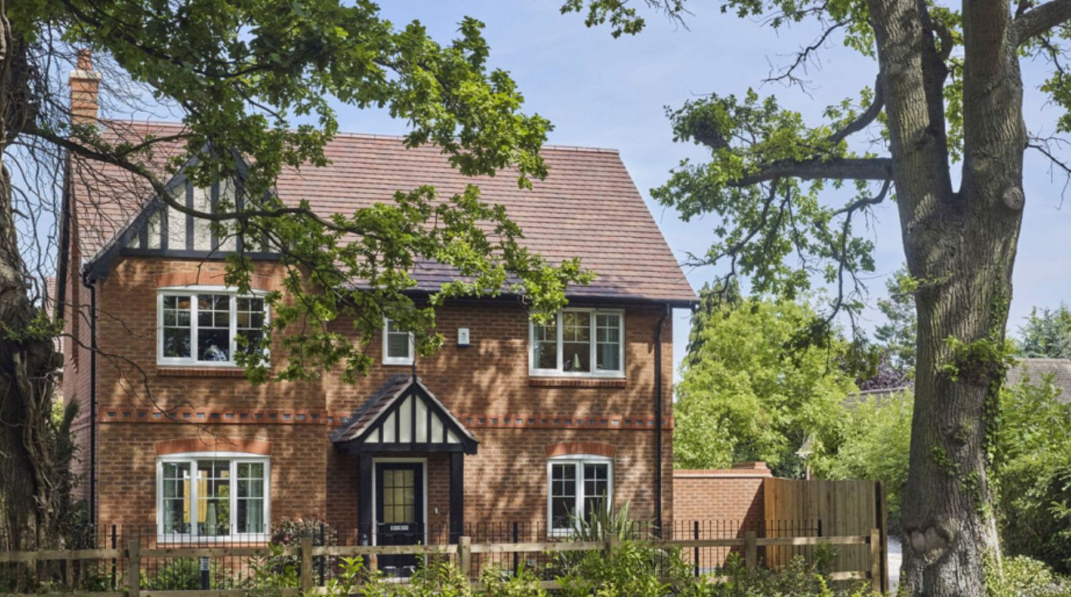 A charming red brick detached house with Tudor-style black and white gabling, surrounded by mature trees and a well-kept garden.