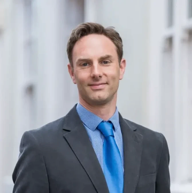 Professional businessman in gray suit and blue tie smiling confidently outdoors.
