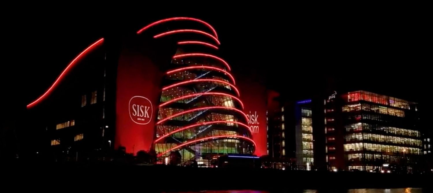The Convention Centre Dublin illuminated in red and orange lights at night, reflecting on the River Liffey.