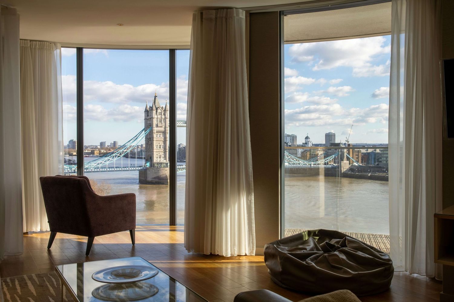 Luxury London apartment living room with floor-to-ceiling windows showcasing iconic Tower Bridge and River Thames views.