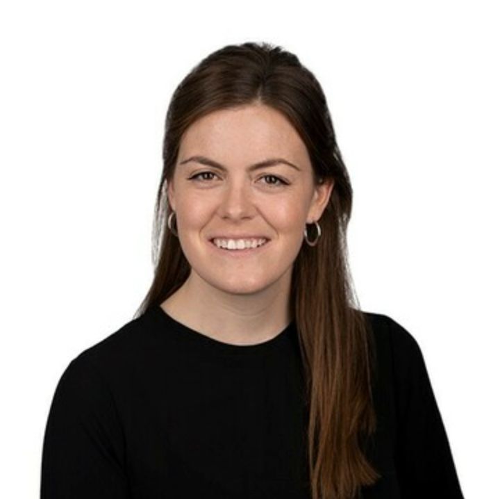 Professional headshot of a smiling young woman with long brown hair wearing a black top against a white background.