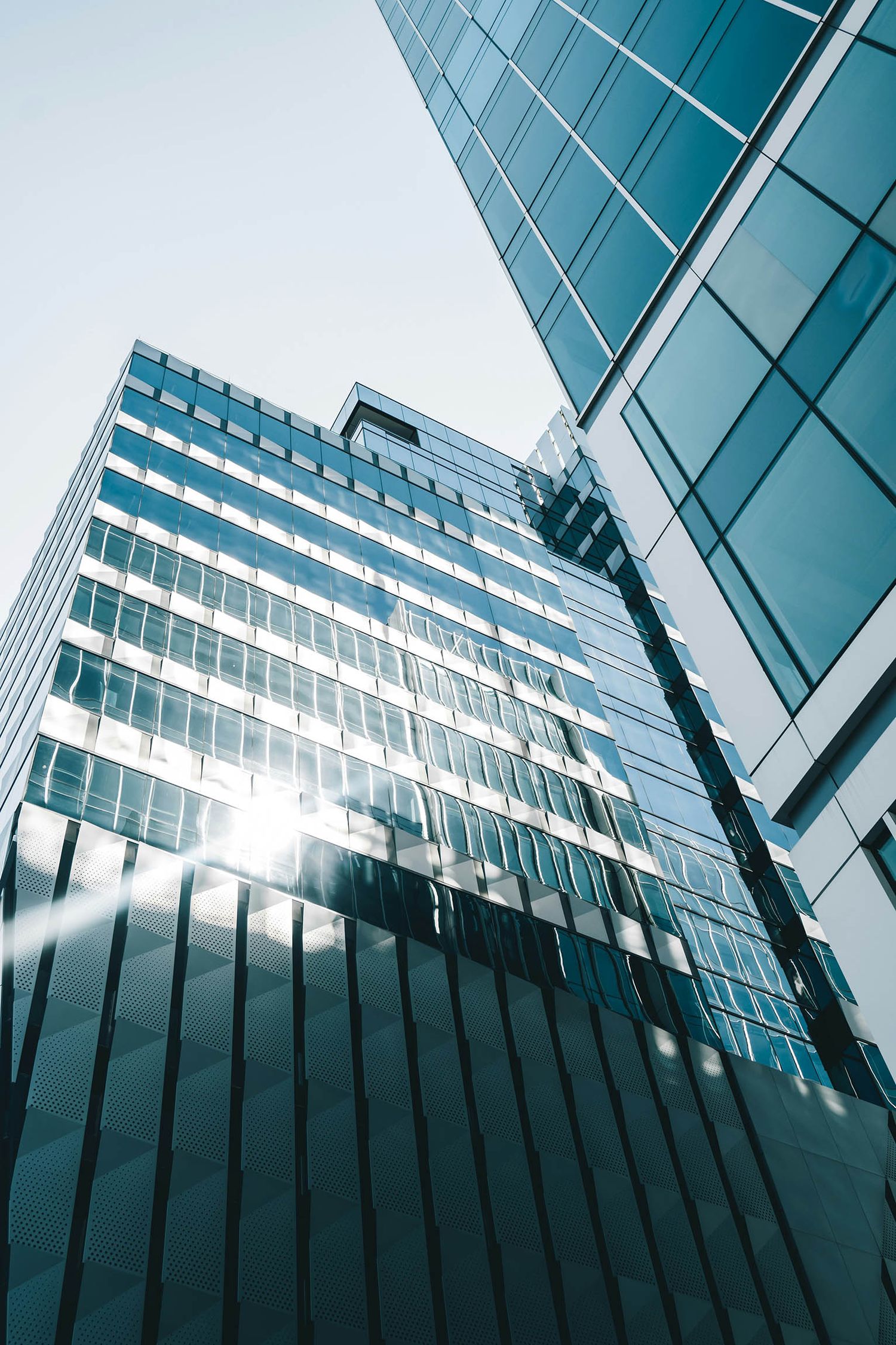 Low-angle view of modern glass skyscrapers reflecting sunlight against a clear blue sky.
