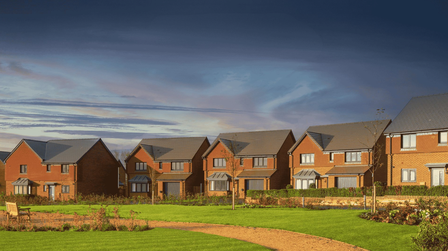 Row of modern brick houses with manicured lawns under dramatic sky in a new residential development.