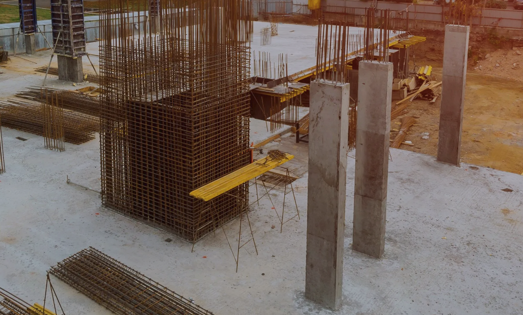Construction site with reinforced concrete columns, rebar frameworks, and yellow scaffolding on a concrete foundation.