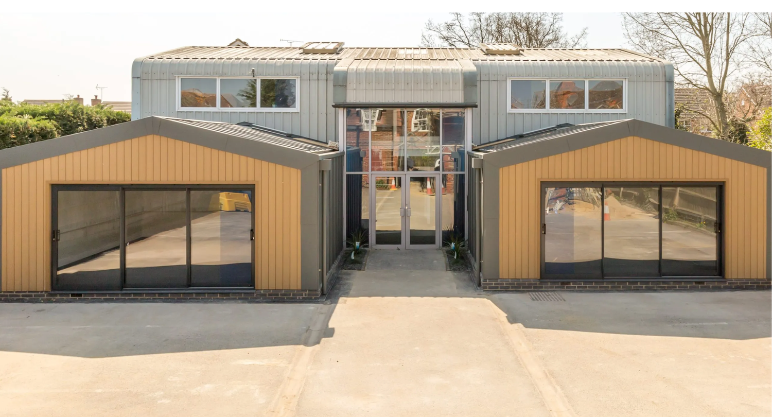 Modern building with gold and grey cladding, large glass sliding doors, and a central entrance on a sunny day.