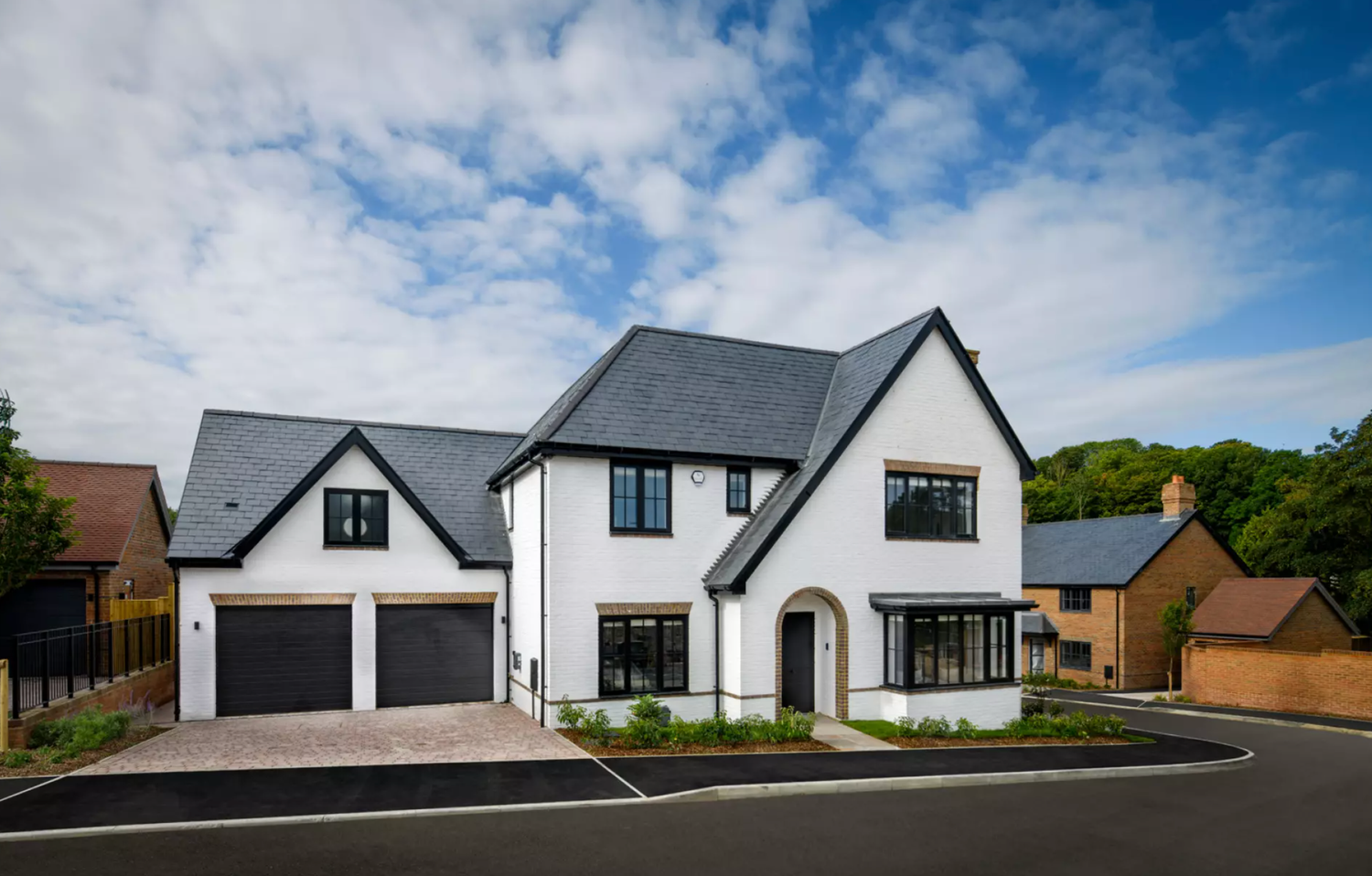 Modern white and black residential houses with pitched roofs line up against a bright blue sky with scattered clouds.
