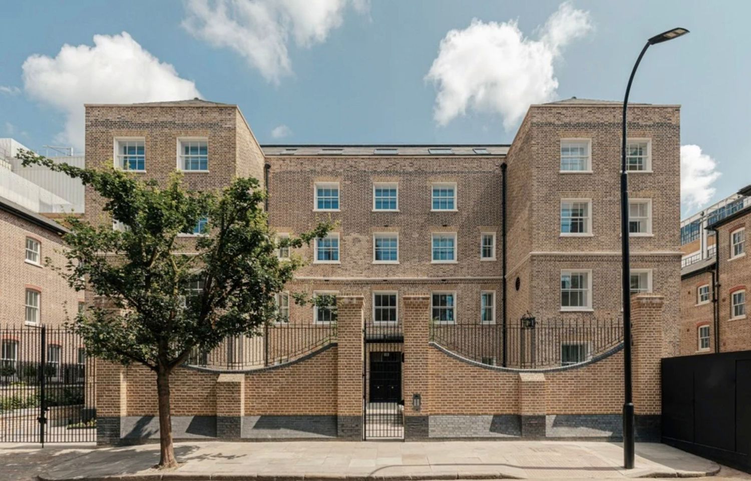 Georgian-style brick apartment building with arched entrance, white sash windows, and mature tree in London.