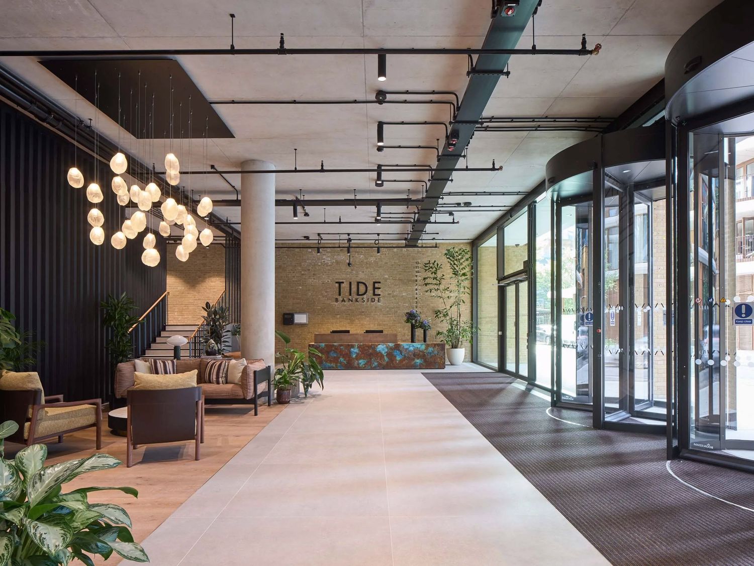 Modern hotel lobby with pendant lighting, lounge seating, exposed ceiling, and floor-to-ceiling windows at Tide.