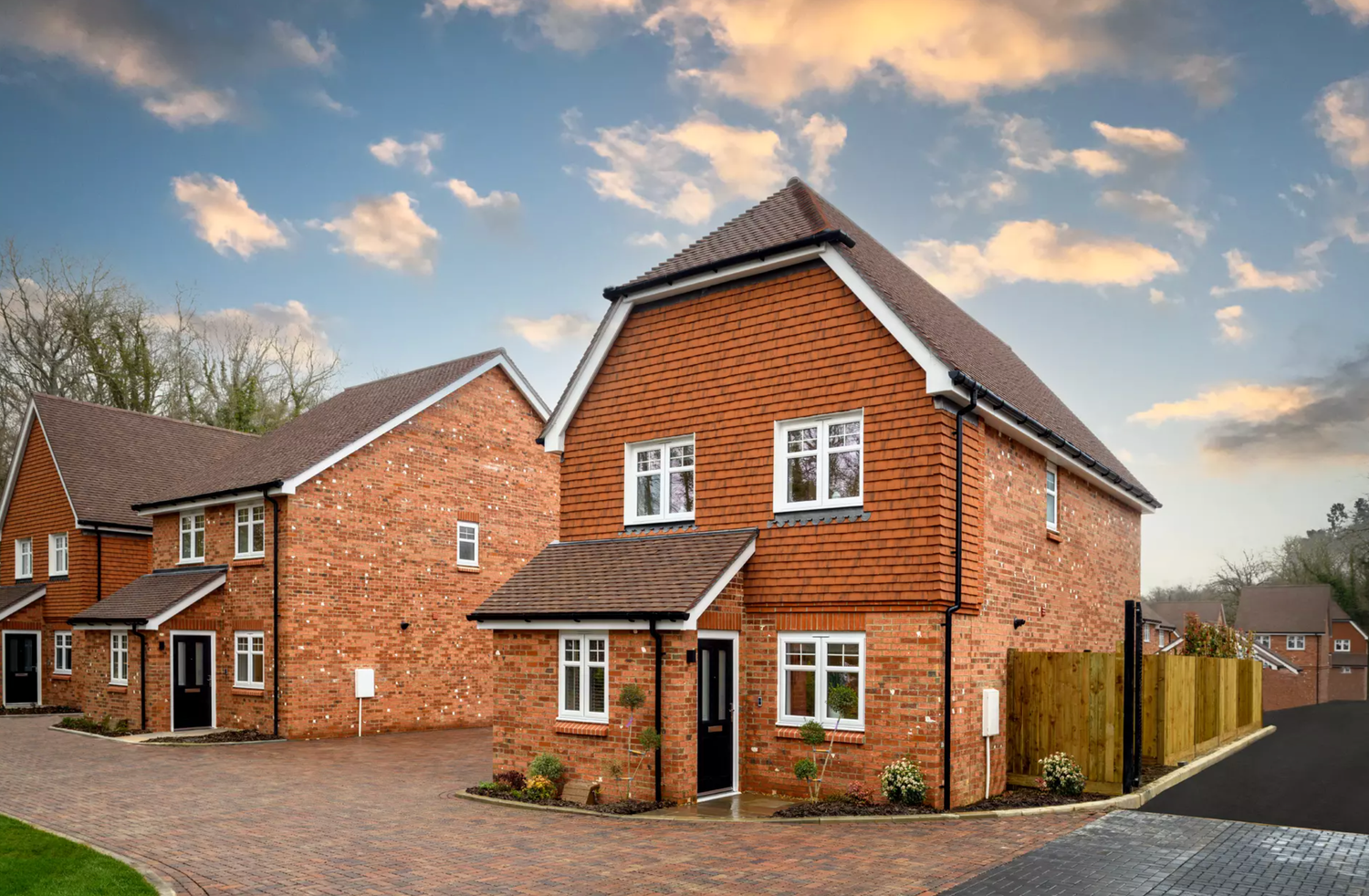 A panoramic view of modern brick homes in a residential development at sunset with dramatic cloudy skies.