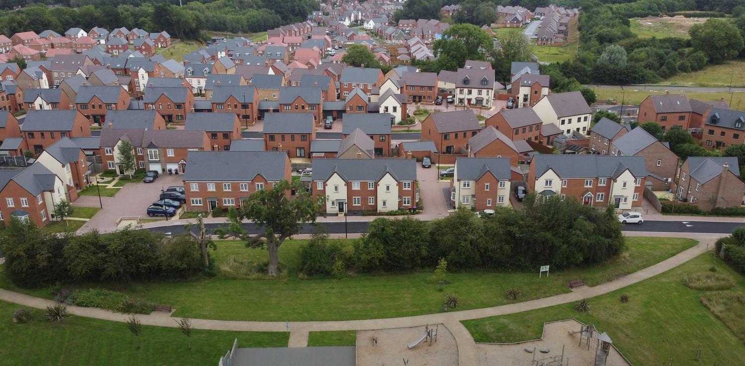 Panoramic aerial view of residential housing developments with red roofs in a suburban neighborhood surrounded by green spaces.