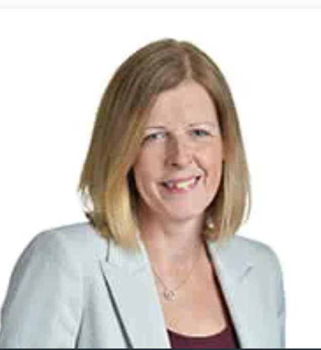 Professional headshot of a smiling woman with blonde hair wearing a light blue blazer and burgundy top.